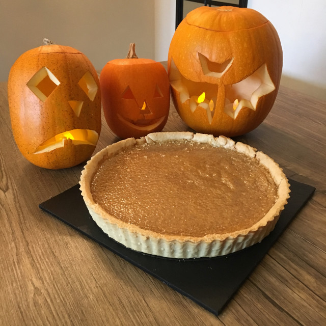 A whole Pumpkin Pie in front of carved pumpkins